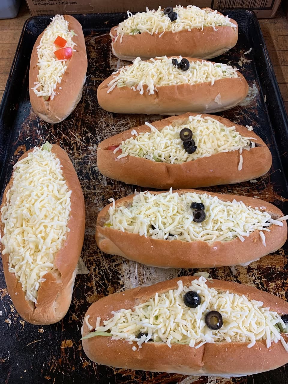 Tray of subs topped with cheese and olives