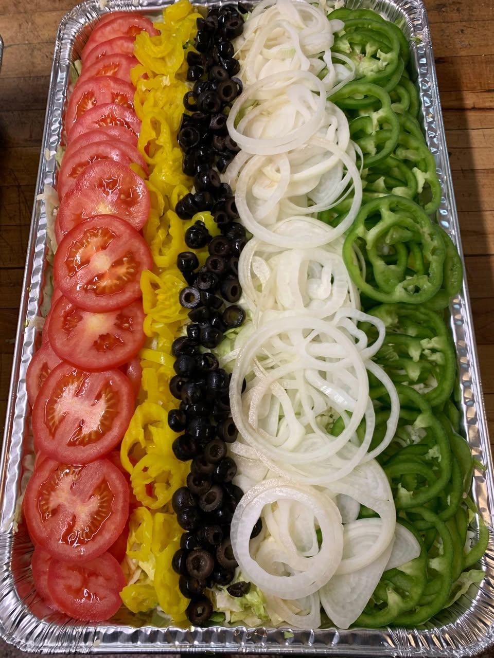 Bulk salad tray with rows of tomato, banana peppers, olives, onions and green peppers