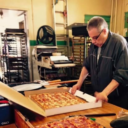 The baker boxing a fresh sheet pizza in the bakery kitchen
